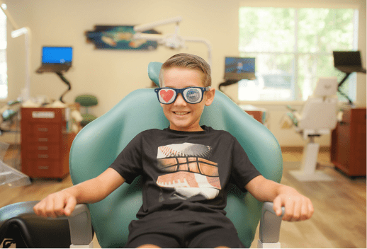 Photo of young patient smiling in a dental chair wearing sunglasses with a heart and Henry Orthodontics logo